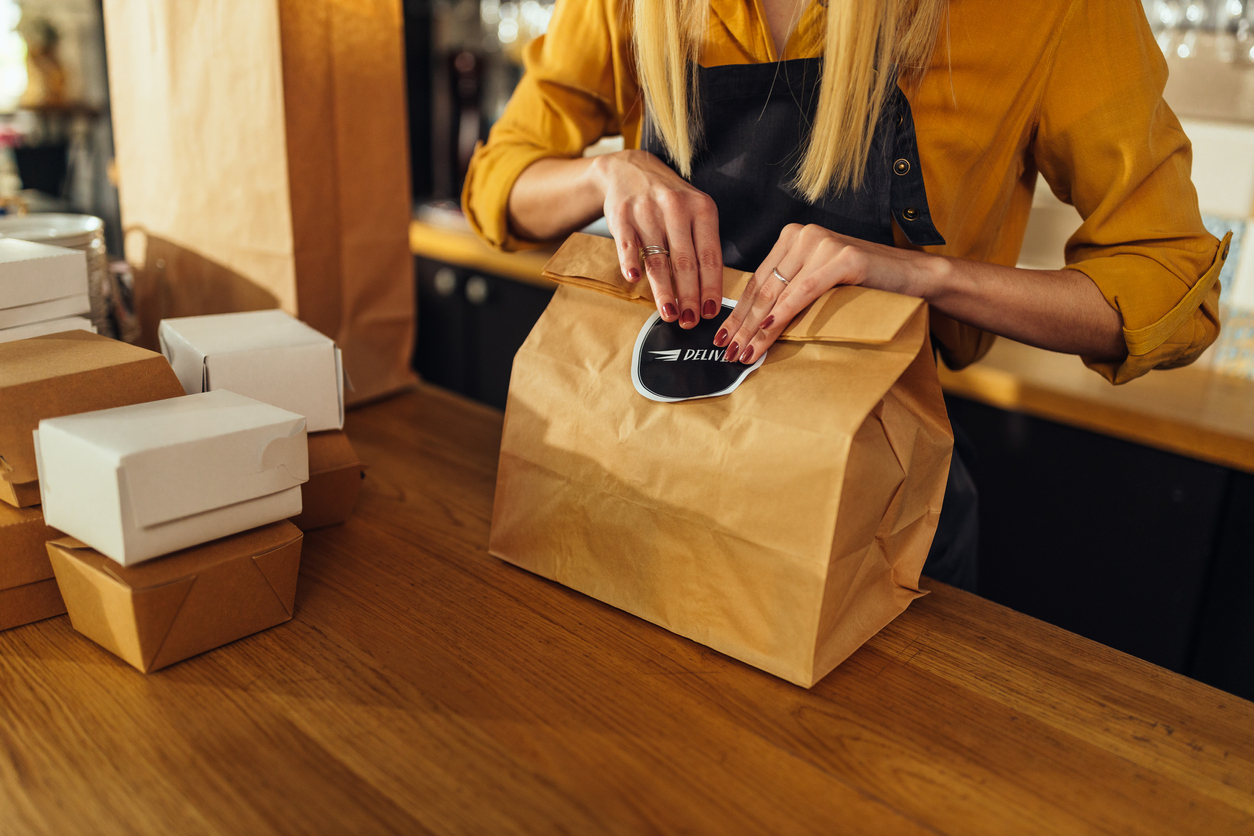 Close up of a hospitality worker packing food in paper bags and preparing them for delivery