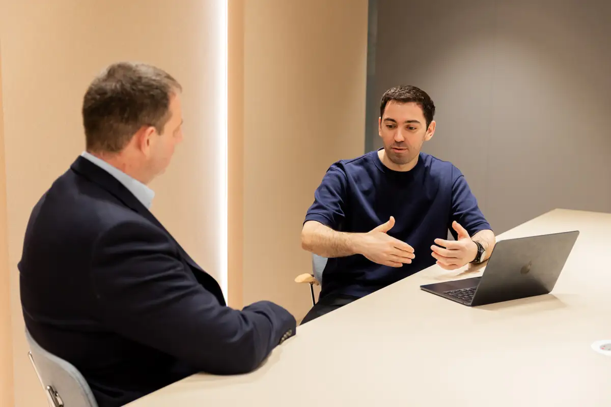 Two men speaking with laptop on table.